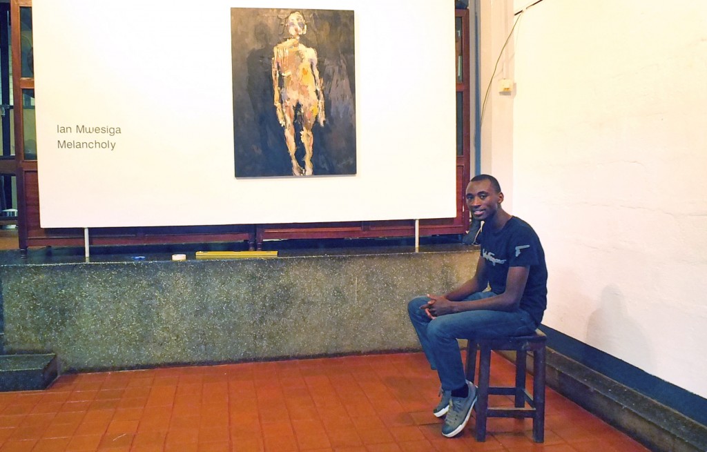 The artist, Ian Mwesiga sits in front of his painting, I am only Human